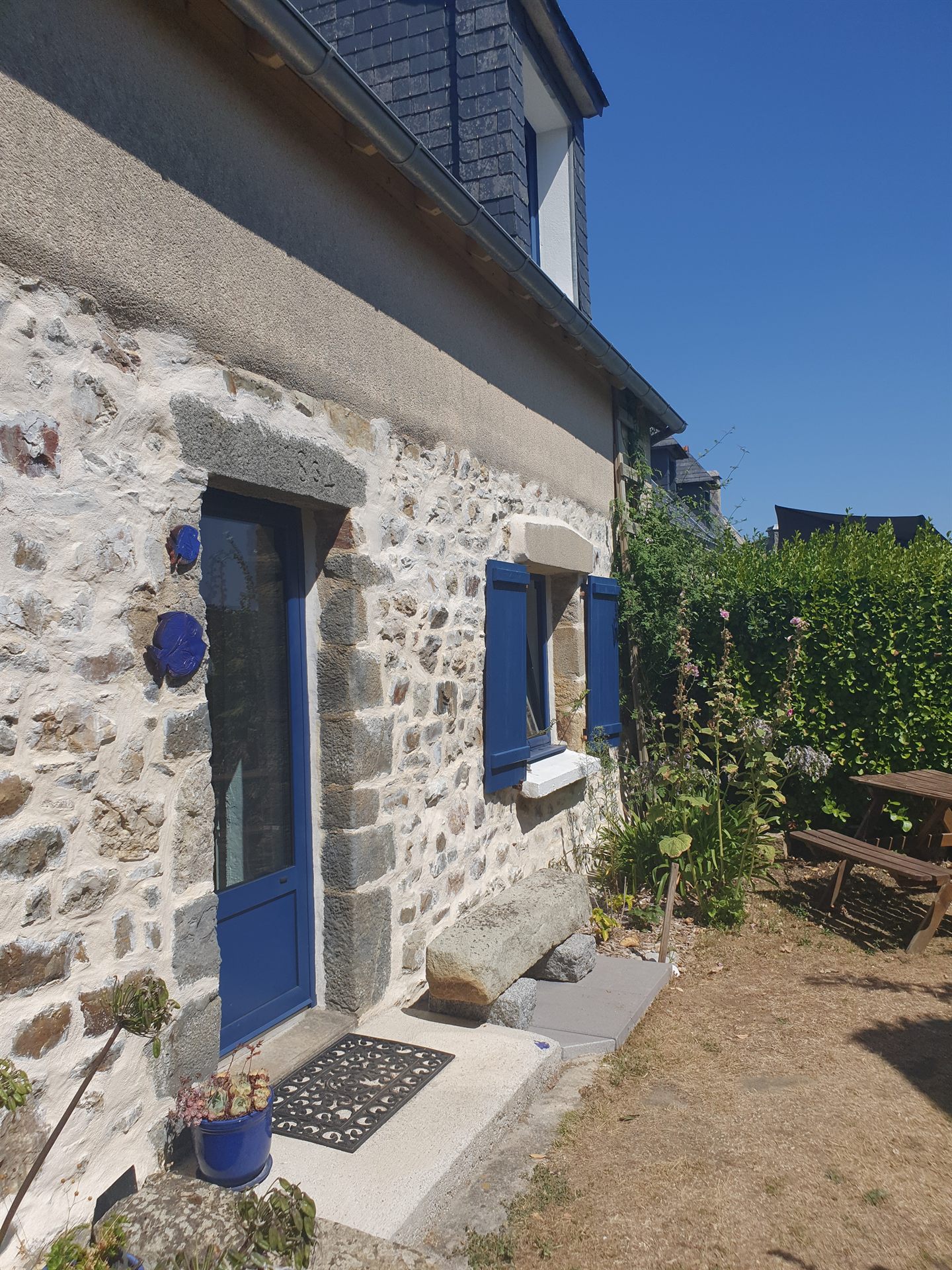 Façade en pierres de Ty Ar Mor avec ses volets bleus, une maison de pêcheur de 1864 à Kersiguenou