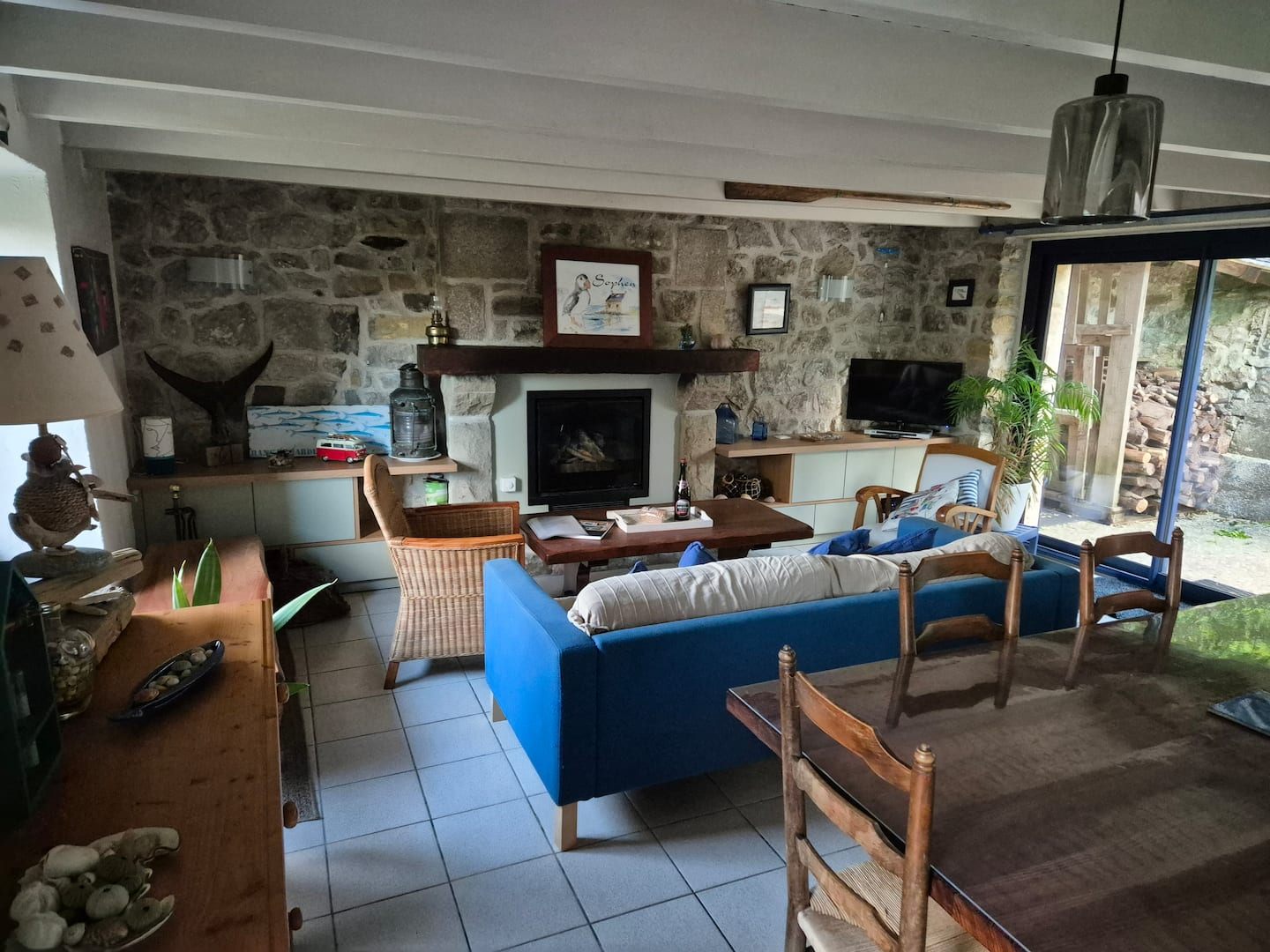 Salon de Ty Ar Mor avec cheminée, mur en pierres apparentes et canapé bleu, à Kersiguenou